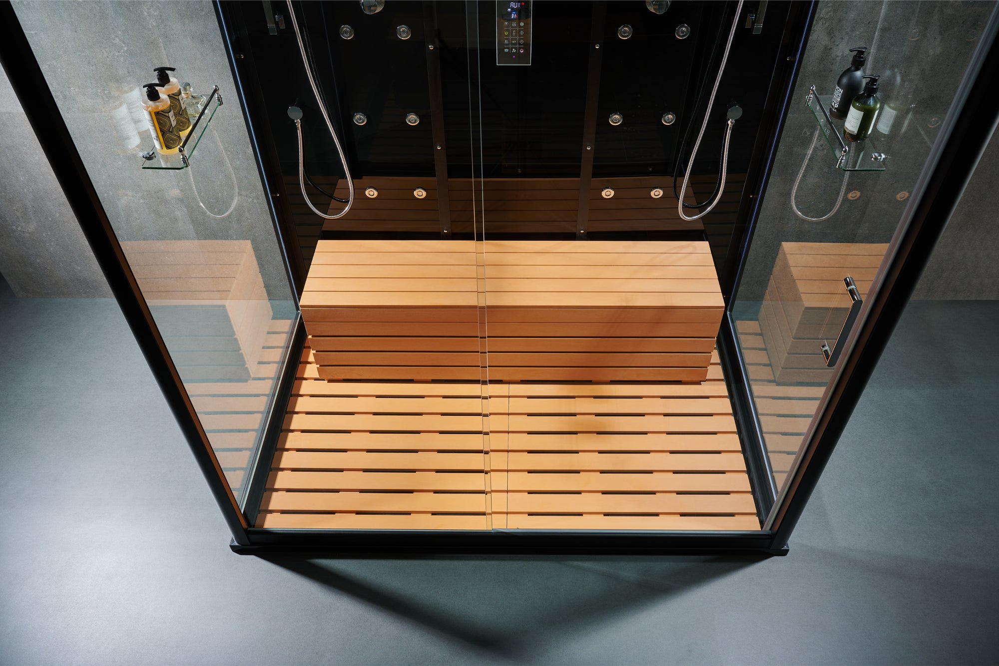 A modern walk-in steam shower cabin with a wooden bench, slatted shower floor, glass walls, and black metal framing, shown from a top-down angle.