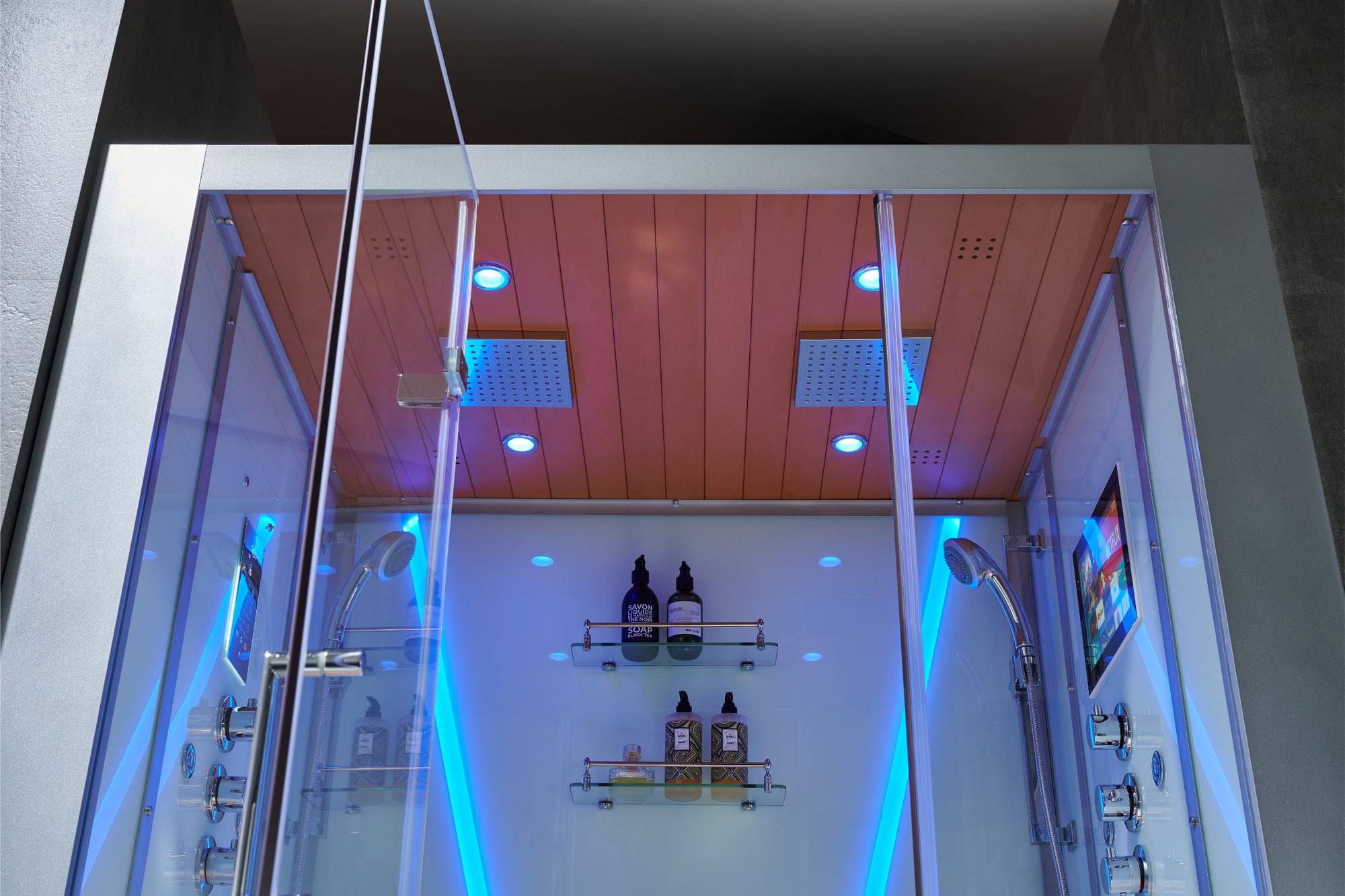 A modern steam shower with rainfall ceiling showers and storage shelving and entertainment screen with shower heads.