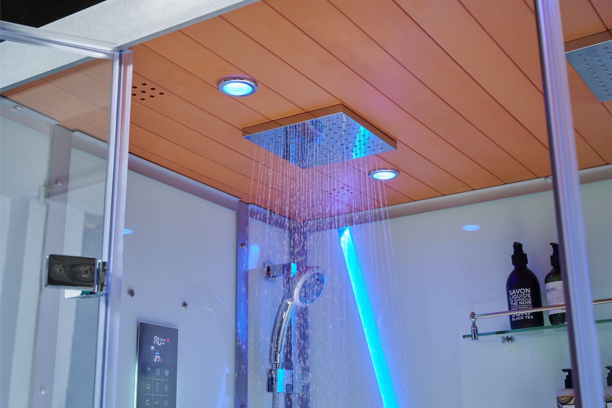A modern shower system with a square rain head mounted on a wood-look ceiling, with water spraying down and blue LED lighting in a bathroom setting.