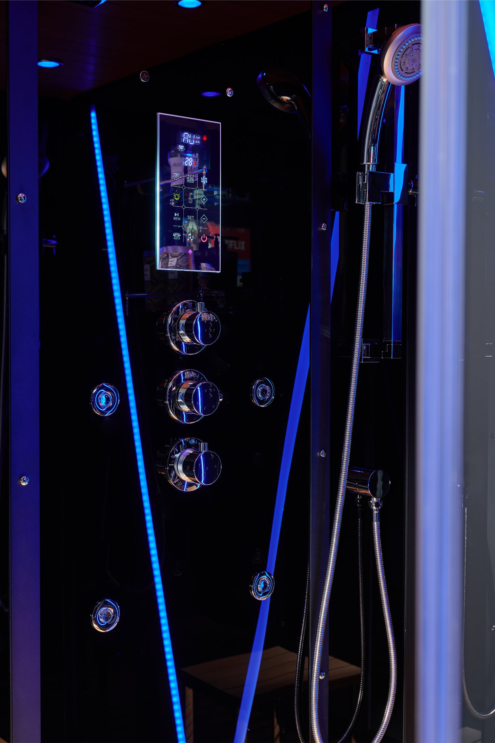 A black modern shower cabin with a digital touch screen, chrome control knobs, and bright blue LED lighting accents, featuring a handheld shower head on the right.