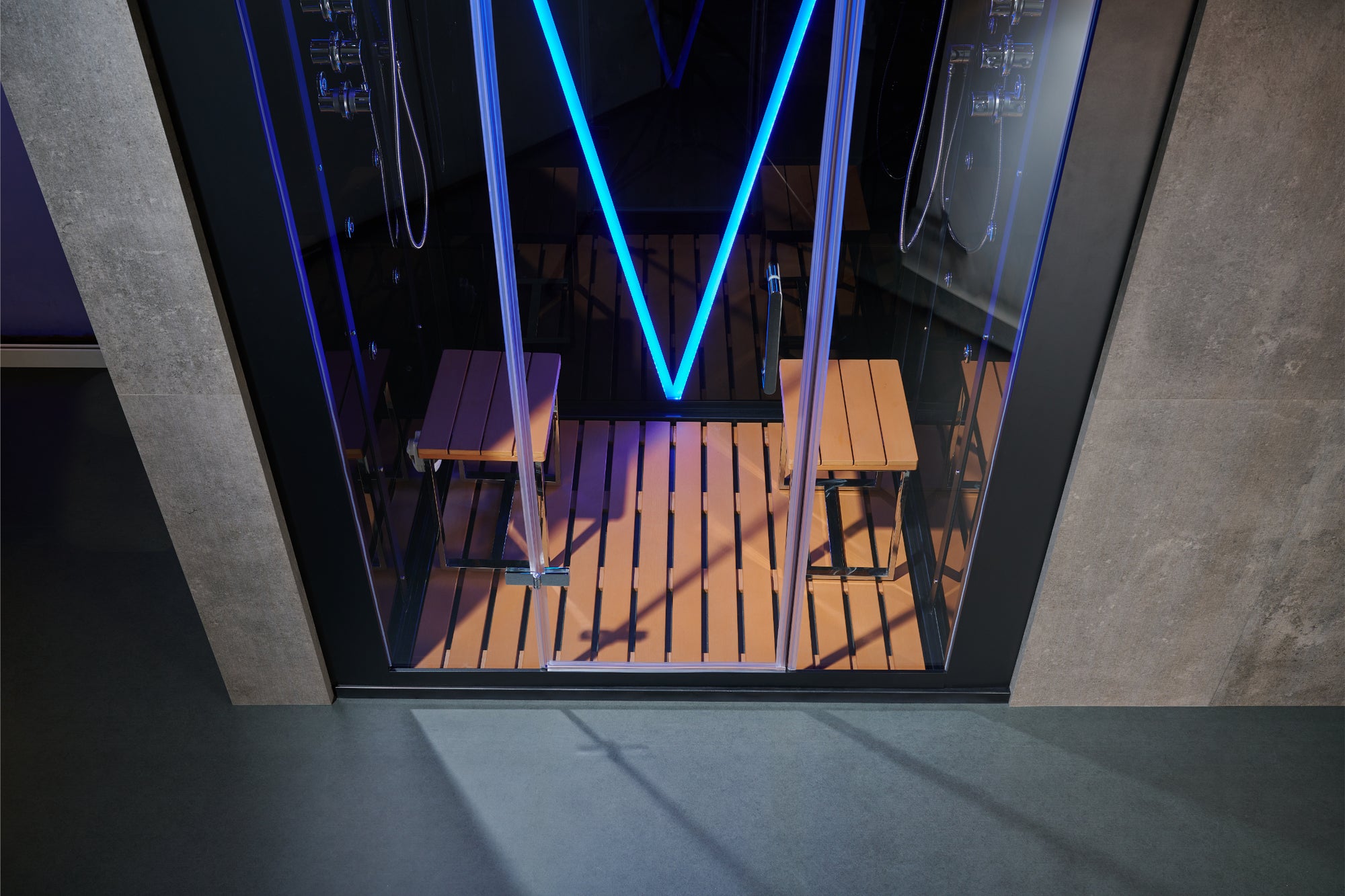 A modern glass steam room or sauna with a black frame, wooden interior floor and benches, and bright blue LED lighting accents.