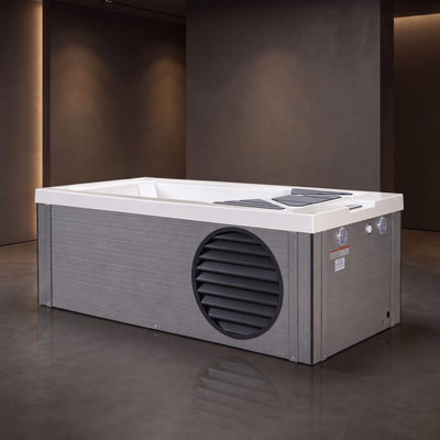 A rectangular outdoor hot tub cold plunge with a white top and gray wood-look exterior, featuring a circular vent on the side and a small control panel, shown in a modern dark-toned patio setting.