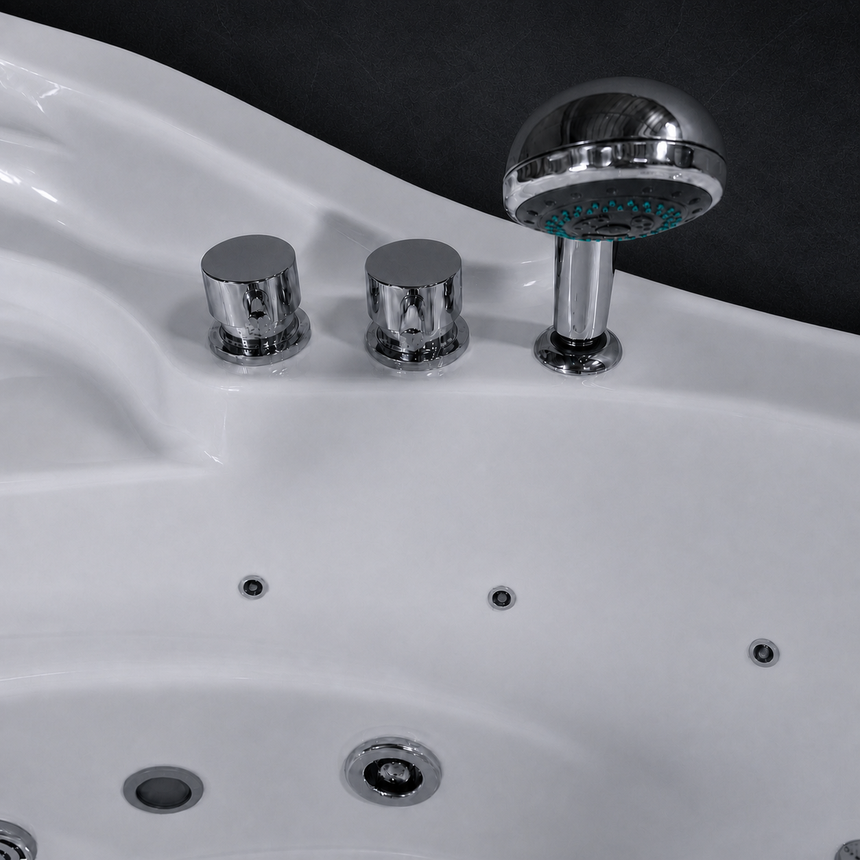 A close-up of a white spa bathtub showing a polished chrome shower head, two cylindrical control knobs, and several jet openings against a dark background.