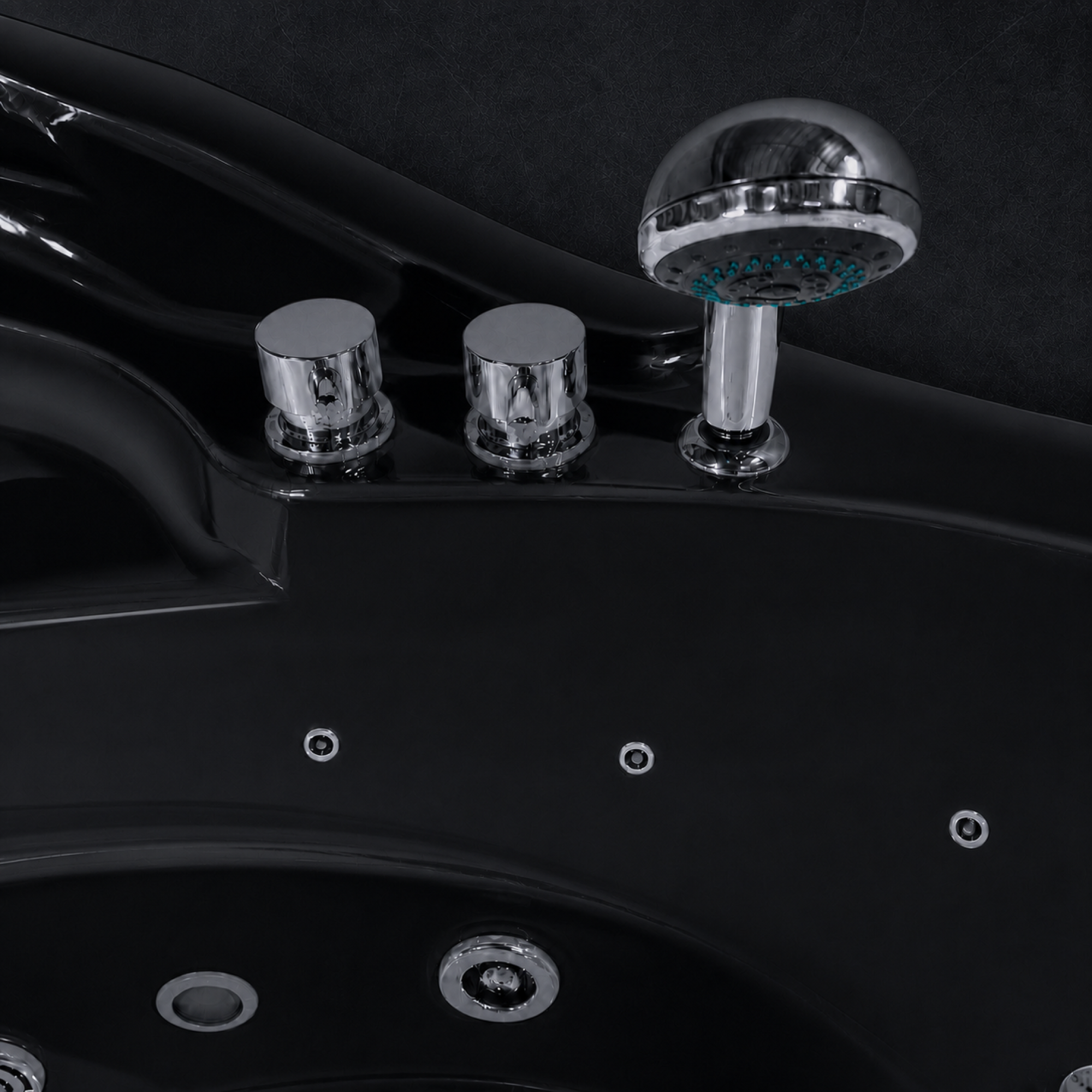 Close-up of a black spa bathtub showing the chrome faucet controls and round shower head against a dark background.